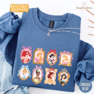A blue sweatshirt with a graphic design featuring illustrations of various Disney princesses.