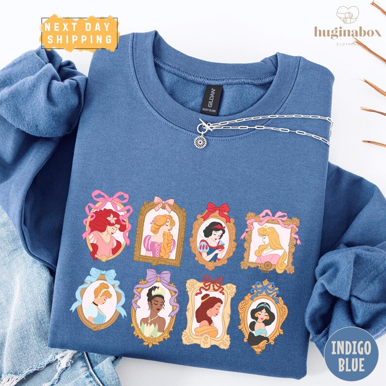 A blue sweatshirt with a graphic design featuring illustrations of various Disney princesses.