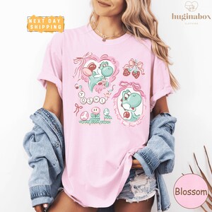 A woman wearing a pink t-shirt with a cartoon character design, a denim jacket, and denim shorts.