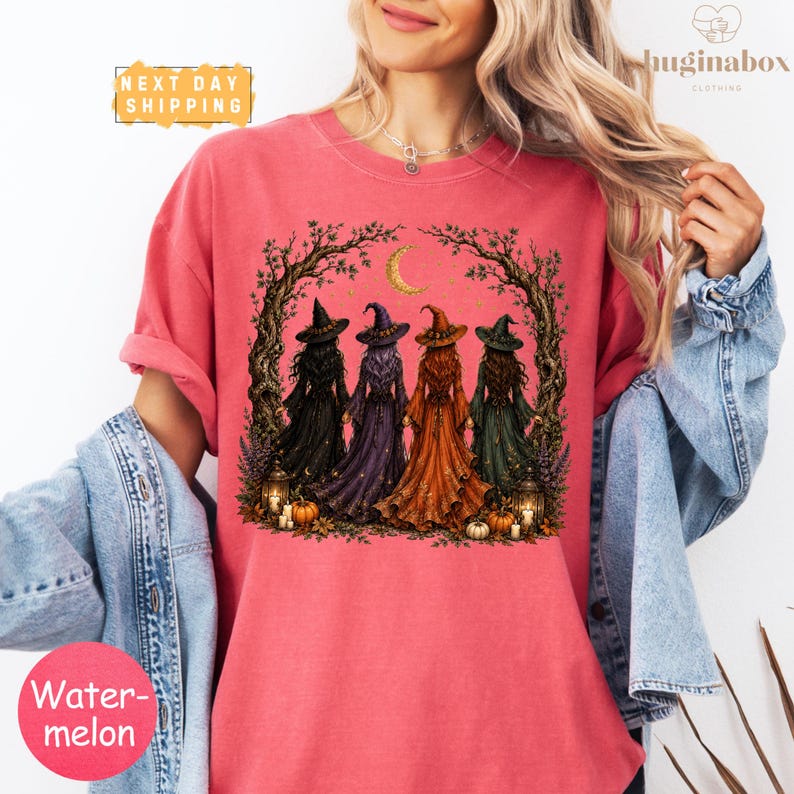 A woman wearing a pink t-shirt with a graphic design of four witch characters surrounded by a tree and a crescent moon.