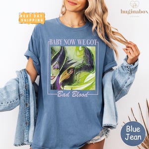 A woman wearing a blue t-shirt with a graphic design and text, posing with her hair in her hair.