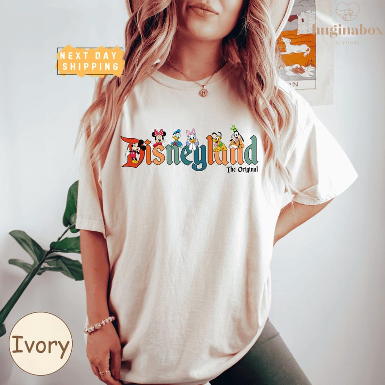 A woman wearing a white t-shirt with the text "Disneyland The Original" printed on it, posing in front of a plant.