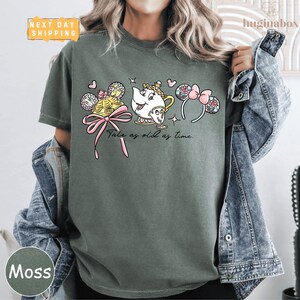 A woman wearing a green t-shirt with a graphic design featuring characters from the Disney film "Beauty and the Beast".