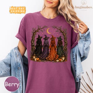 A woman wearing a purple t-shirt with a graphic design of four witch characters in a forest setting.