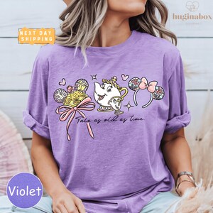 A woman wearing a purple t-shirt with a Disney character design, including a teapot, a character with a headband, and a character with a bow.