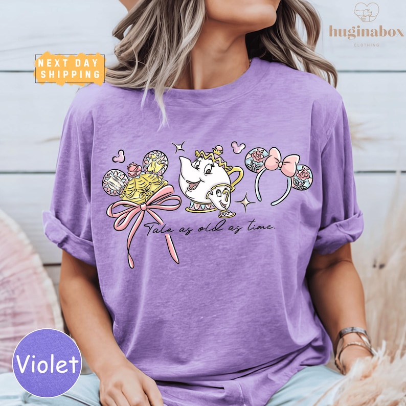 A woman wearing a purple t-shirt with a Disney character design, including a teapot, a character with a headband, and a character with a bow.