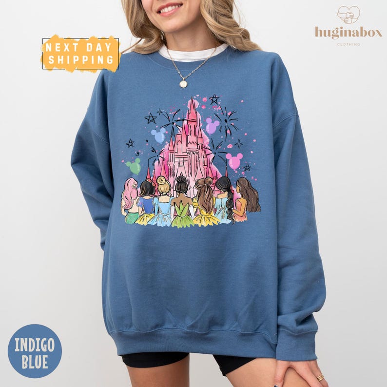 A woman wearing a blue sweatshirt with a colorful illustration of Disney princesses and a castle on it.