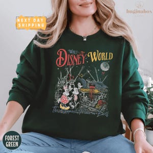 A woman wearing a green sweater with a Disney World-themed graphic printed on it.