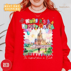 A person wearing a red sweater with a colorful, whimsical design depicting a Disney World castle and various Disney characters.