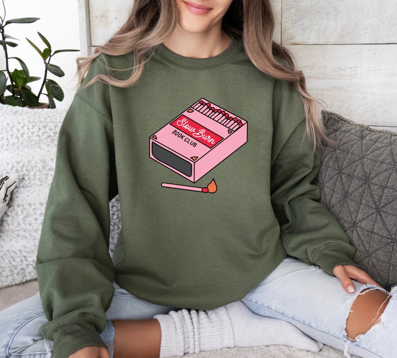 May include: A green sweatshirt with a pink box of matches that says "Slow Burn Book Club" and a lit match on the front.