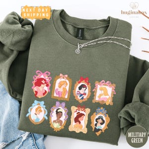 A green sweatshirt with a graphic design featuring illustrations of various Disney princesses.