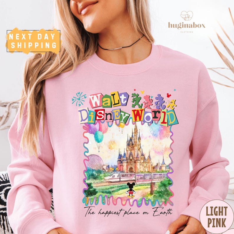 A woman wearing a pink sweatshirt with a colorful illustration of Walt Disney World and the text "The happiest place on Earth".