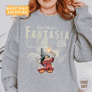 A person wearing a gray sweatshirt with a Disney-themed graphic of a wizard character from the movie "Fantasia".