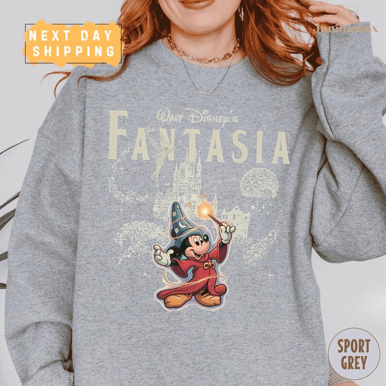 A person wearing a gray sweatshirt with a Disney-themed graphic of a wizard character from the movie "Fantasia".