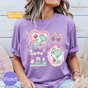 A woman wearing a purple t-shirt with a colorful graphic design featuring characters from the video game series Yoshi.