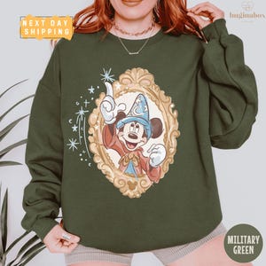 A person wearing a green sweatshirt with a Mickey Mouse design and a framed illustration of a wizard.