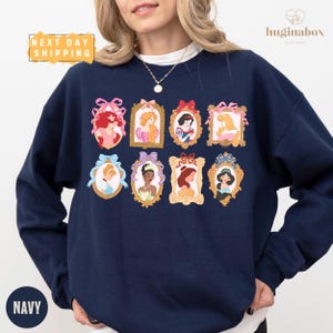 A woman wearing a navy blue sweatshirt with a collage of illustrations of Disney princesses on it.