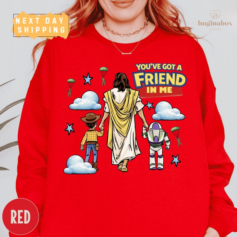 A red sweater with a cartoon illustration of a person holding a Bible and a toy robot, along with the text "You've got a Friend in Me" and a cloud with a star.