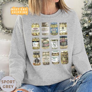 a woman sitting on a couch wearing a sweatshirt with a picture of jars of pick