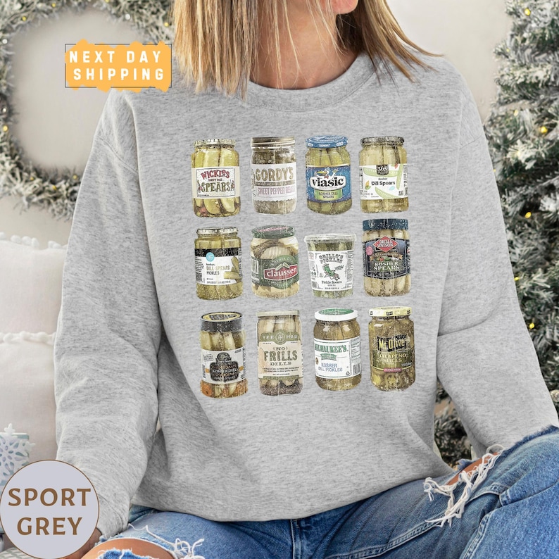 a woman sitting on a couch wearing a sweatshirt with a picture of jars of pick