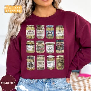 a woman wearing a maroon sweatshirt with jars of pickles on it