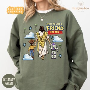 A green sweatshirt with a graphic design depicting a person in a yellow robe and a child, along with a character from the Toy Story franchise.