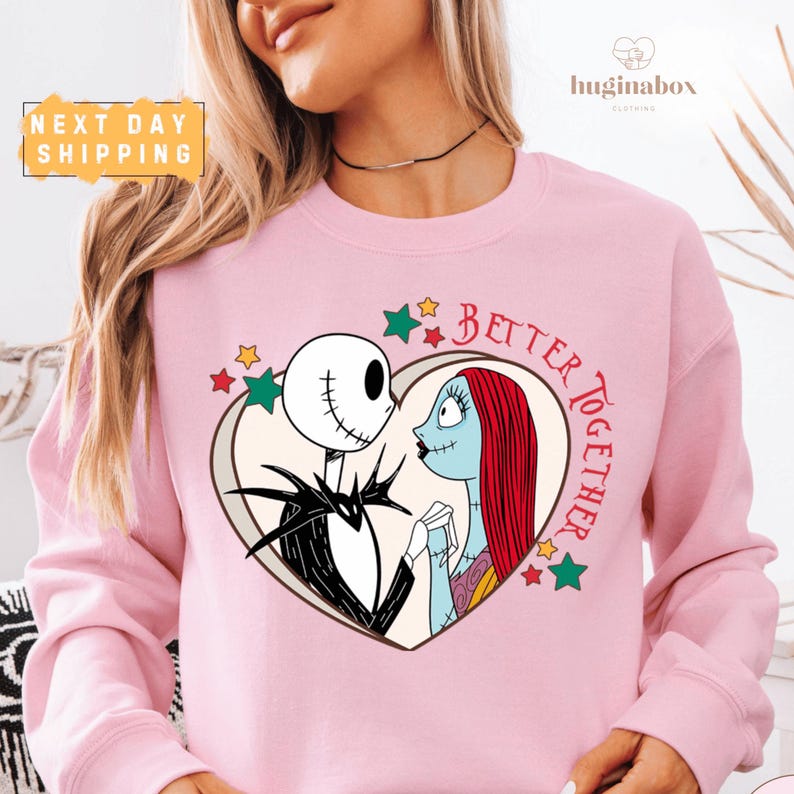 A woman wearing a pink sweatshirt with a graphic design featuring the characters Jack Skellington and Sally from the movie "Jack Skellington and Sally".