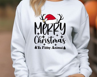 Op de afbeelding: Witte trui met een zwart grafisch ontwerp met de tekst "Merry Christmas Ya Filthy Animal" met een rode kerstmanmuts en rendiergewei.