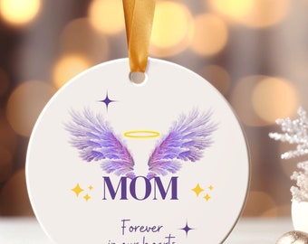 Op de afbeelding: Ronde witte ornament met paarse engelenvleugels, een gouden halo en de tekst "MOM Forever in our hearts" met gouden sterren.