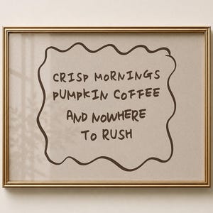 Könnte beinhalten: Ein rechteckiger Wandkunstdruck in einem metallisch goldenen Rahmen mit beigem Hintergrund und einem dunkelbraunen, handgezeichneten wellenförmigen Rand. Der dunkelbraune Text lautet: CRISP MORNINGS PUMPKIN COFFEE AND NOWHERE TO RUSH, zentriert.