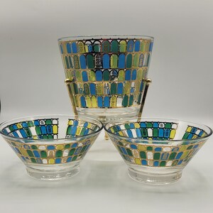 May include: A set of three vintage glass bowls with a gold rim and a geometric pattern of blue, green, and yellow arches. The bowls are on a gold metal stand.