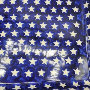 Op de afbeelding: Rechthoekige keramische ovenschaal met een blauwe achtergrond en een patroon van witte sterren. De schaal heeft een cr&egrave;mekleurige rand en een glanzende afwerking. Het sterrenpatroon is gelijkmatig verdeeld.