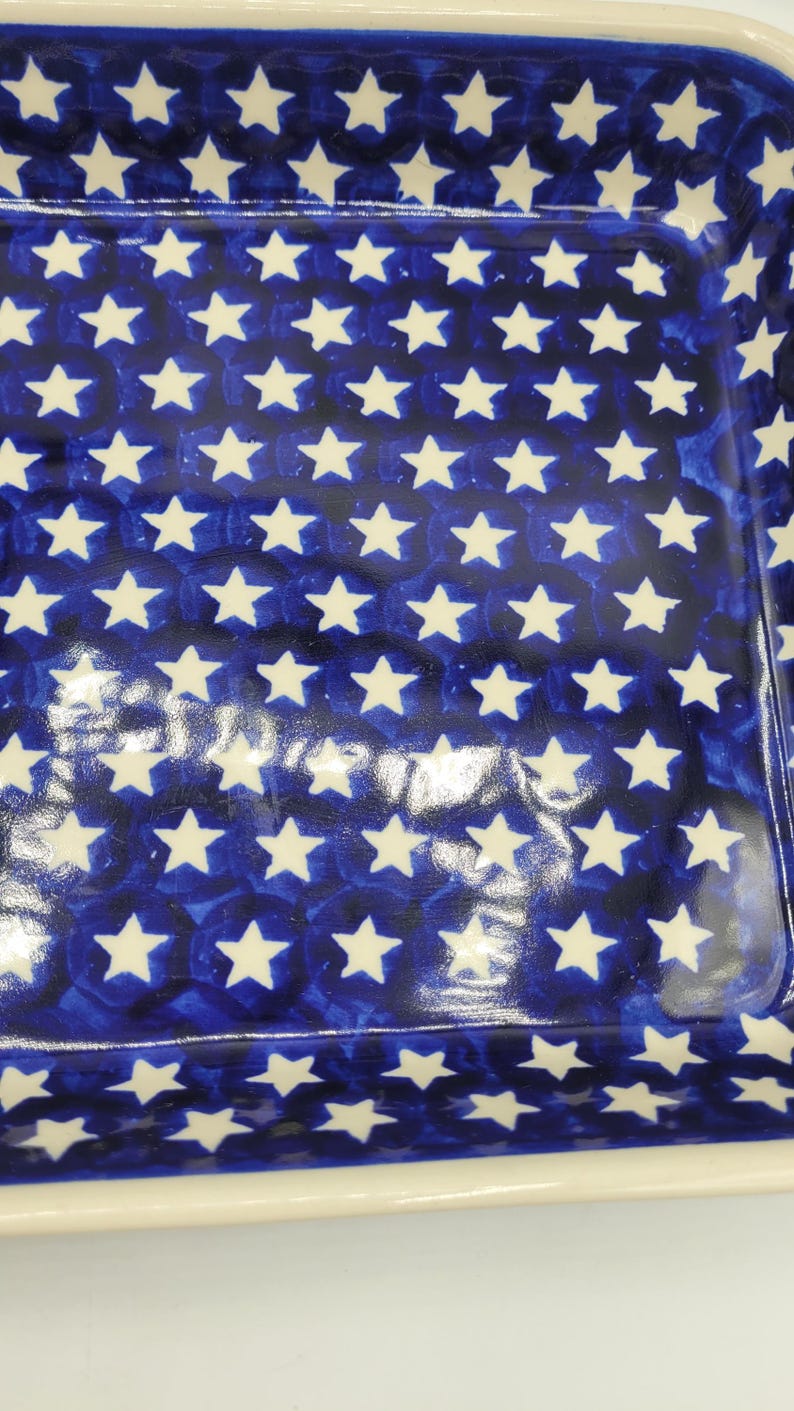 Op de afbeelding: Rechthoekige keramische ovenschaal met een blauwe achtergrond en een patroon van witte sterren. De schaal heeft een cr&egrave;mekleurige rand en een glanzende afwerking. Het sterrenpatroon is gelijkmatig verdeeld.