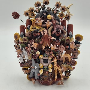 May include: A detailed, hand-painted ceramic tree of life sculpture. The sculpture features various animals, figures, and floral elements in shades of brown, orange, yellow, and white. A zebra, giraffe, and elephant are among the animals depicted.