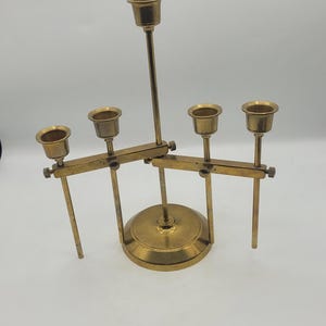 May include: A brass candle holder with five candle cups. The base is round, and the arms extend horizontally with adjustable candle holders. The overall design is vintage and decorative.