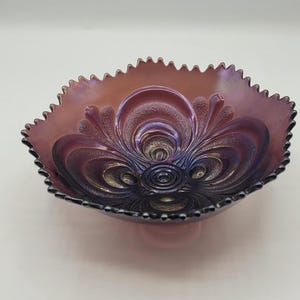 May include: A purple iridescent glass bowl with a scalloped edge and a floral design. The bowl has a deep purple hue with hints of blue and gold.