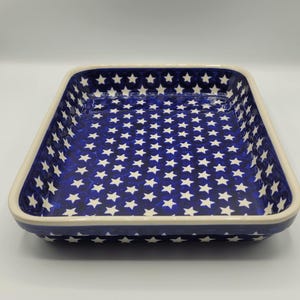 Op de afbeelding: Rechthoekige keramische ovenschaal met een marineblauw interieur met een wit sterrenpatroon. De rand is cr&egrave;mekleurig. Geschikt om in te bakken en te serveren.