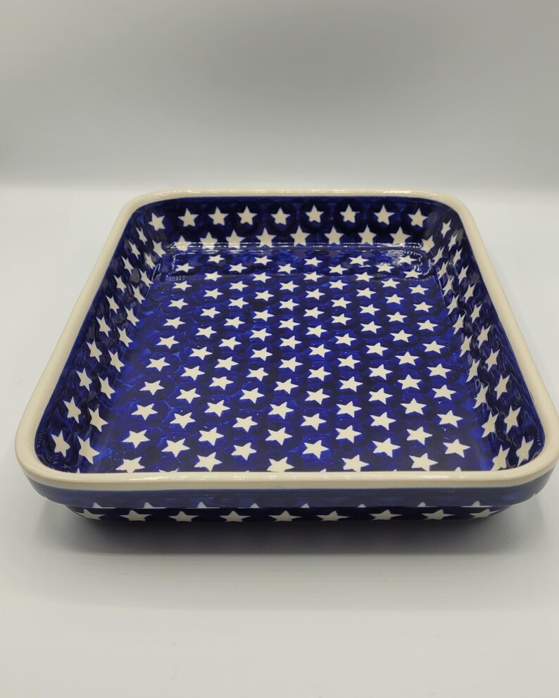 Op de afbeelding: Rechthoekige keramische ovenschaal met een marineblauw interieur met een wit sterrenpatroon. De rand is cr&egrave;mekleurig. Geschikt om in te bakken en te serveren.