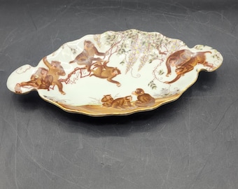 Plato decorativo de porcelana china vintage con diseño de monos alegres y glicinias, con asas festoneadas y detalles dorados.