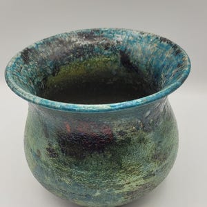 May include: A small, round, ceramic pot with a teal, green, and black glaze. The pot has a slightly flared rim and a rounded bottom.
