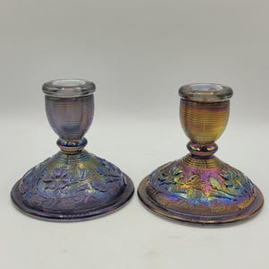 Puede incluir: Dos candelabros de vidrio iridiscente. Los candelabros tienen una base redonda con un diseño floral y una parte superior cilíndrica. Los colores cambian de púrpura a dorado. Los candelabros miden aproximadamente 13 cm de alto.