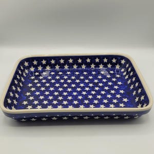 Op de afbeelding: Rechthoekige keramische ovenschaal met een marineblauwe achtergrond en een patroon van witte sterren. De schaal heeft een cr&egrave;mekleurige rand en is geschikt om in te bakken en te serveren. De schaal is ongeveer 30 cm lang en 20 cm breed.