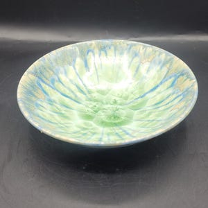 May include: A ceramic bowl with a light green interior and a blue and green exterior. The bowl has a textured surface and a round shape. The bowl is likely handmade and suitable for serving food.