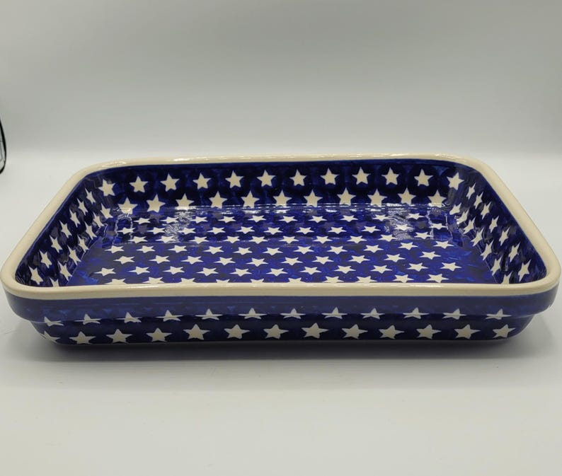 Op de afbeelding: Rechthoekige keramische ovenschaal met een blauwe achtergrond en een wit sterrenpatroon. De schaal heeft een cr&egrave;mekleurige rand en is ontworpen om in te bakken en te serveren. Het sterrenpatroon voegt een decoratief tintje toe.