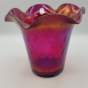 May include: An iridescent glass vase with a ruffled edge. The vase has a colour gradient from magenta to gold, with a textured pattern. A small sticker is visible near the rim.
