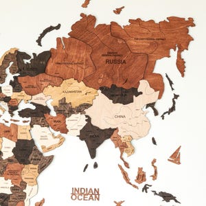 May include: A wooden world map in shades of brown, tan, and black, with country outlines and names. The words "INDIAN OCEAN" are visible. Includes small wooden airplane and sailboat decorations.