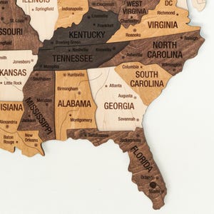 May include: A wooden map of the United States with each state outlined in a different shade of brown. The states are labeled with their names and major cities are marked with dots.
