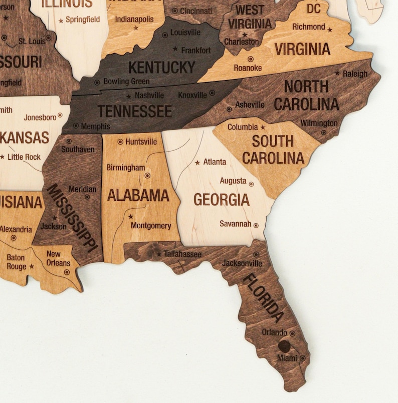 May include: A wooden map of the United States with each state outlined in a different shade of brown. The states are labeled with their names and major cities are marked with dots.