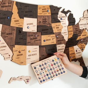 May include: A wooden map of the United States with each state outlined and labeled. The map is decorated with small, colorful flags representing each state. The flags are arranged in a grid on a separate wooden board labeled "USA States Flags".