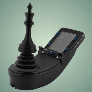 May include: A black joystick with a black chess king piece on top. The joystick has a small screen and buttons.